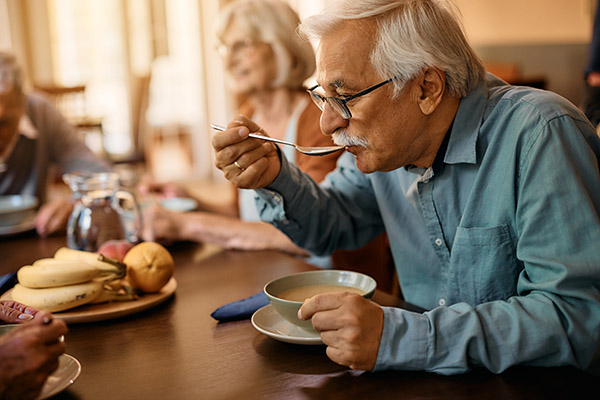 Senior man eats soup while having lunch at residential care home Senior man eats soup while having lunch at residential care home